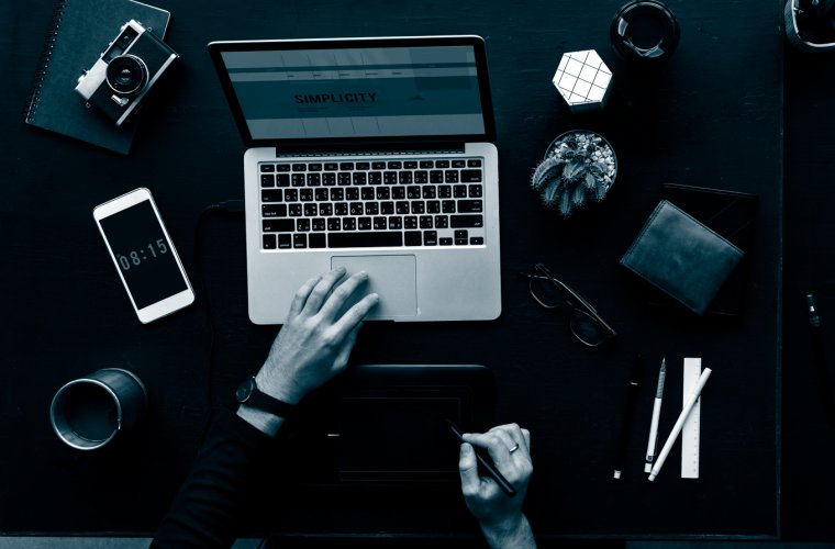 Overhead view of a desk with a laptop, camera, notebook and phone